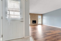 Entryway with a paneled door featuring decorative glass inserts, opening to an interior space with wood-finish flooring, a contemporary fireplace with a stone-finish surround, and a light blue painted wall - 