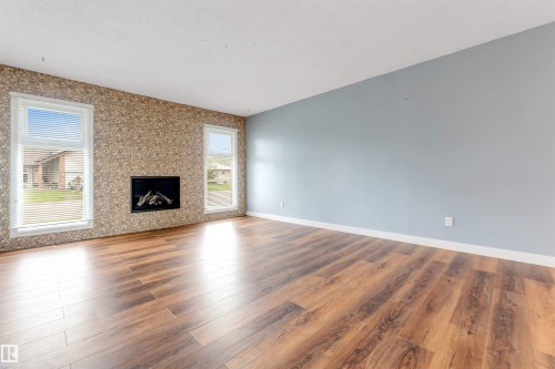 Spacious interior room featuring wood-finish flooring, a textured accent wall with a built-in fireplace, and two tall windows - 193 Woodvale Road W, Edmonton, AB 