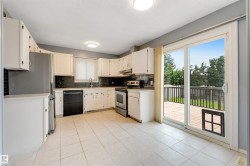 Kitchen featuring white cabinetry, dark tile backsplash, stainless steel refrigerator, black dishwasher, and a sliding glass door opening to an outdoor deck - 