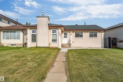 Stucco exterior featuring a dark asphalt shingle roof, a prominent chimney structure, multiple windows, and a concrete pathway leading to the front entry - 