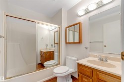 Full bathroom featuring a white tub with sliding glass doors, a single vanity with wood-finish cabinetry and a light-toned countertop, a wall-mounted mirror, and a wood-framed medicine cabinet - 