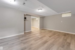 Spacious room featuring light wood-finish flooring, neutral wall tones, white baseboards, and a suspended acoustic ceiling - 