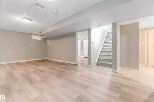 Spacious lower-level area featuring wood-finish flooring, neutral wall tones, a drop ceiling with recessed lighting, and a visible staircase - 193 Woodvale Road W, Edmonton, AB 