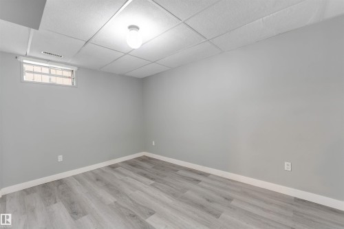 Spacious interior room featuring light gray walls, wood-finish flooring, a drop ceiling with recessed lighting, and a horizontal window with white trim - 193 Woodvale Road W, Edmonton, AB 