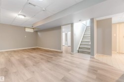 Spacious lower-level area featuring wood-finish flooring, neutral wall tones, a drop ceiling with recessed lighting, and a visible staircase - 