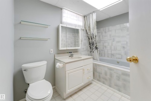 Full bathroom featuring a white vanity with integrated sink, coordinating toilet, and a tiled tub surround - 193 Woodvale Road W, Edmonton, AB 