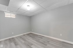 Spacious interior room featuring light gray walls, wood-finish flooring, a drop ceiling with recessed lighting, and a horizontal window with white trim - 
