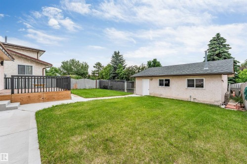 Expansive backyard featuring a manicured lawn, concrete pathway, and a large wood deck with dark railings - 193 Woodvale Road W, Edmonton, AB 