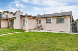Stucco exterior with a peaked roofline, featuring a front porch with railing, a prominent chimney, and a chain-link fence at the property edge - 