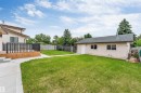 Expansive backyard featuring a manicured lawn, concrete pathway, and a large wood deck with dark railings - 193 Woodvale Road W, Edmonton, AB 