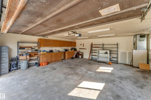 Spacious two-car garage featuring a concrete floor, extensive built-in cabinetry, additional shelving, fluorescent lighting, and a window for natural light - 193 Woodvale Road Nw, Edmonton, AB - Indoor Photo Showing Garage