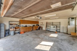 Spacious two-car garage featuring a concrete floor, extensive built-in cabinetry, additional shelving, fluorescent lighting, and a window for natural light - 