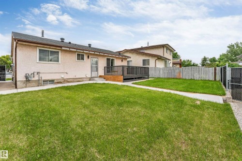 Expansive rear yard featuring green lawn, a concrete pathway, a dark wood-finish deck with railings, and a chain-link fence with a gate - 193 Woodvale Road W, Edmonton, AB 