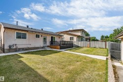 Rear exterior featuring a spacious lawn, concrete walkways, a dark wood-finish deck, and a privacy fence - 