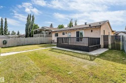 Expansive backyard featuring a concrete patio, a dark wood deck with matching railing, and a chain-link fence on one side - 