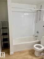 White tiled bath with shower and light wood-finish flooring - 