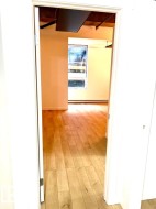 Light wood-finish flooring extending into an open room with a large window and exposed ceiling beams - 