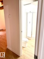 Bathroom featuring a corner shower enclosure, white commode, and light wood-finish flooring - 