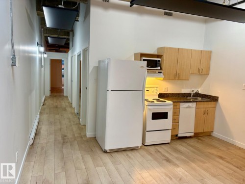 Kitchenette with wood-finish flooring, light-colored cabinetry, dark countertops, and white appliances including a refrigerator, stove, and dishwasher - 206 10024 Jasper Avenue, Edmonton, AB 
