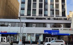 Multi-story building featuring a facade of white and black panels, multiple windows, and a ground-level retail presence with blue awnings - 
