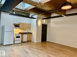 Open-concept living area featuring wood-finish flooring, a kitchen with light wood cabinetry, white appliances, and a dark countertop - 