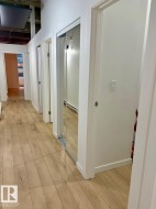 Hallway featuring wood-finish flooring, white walls, multiple doorways, and a mirrored sliding closet door - 