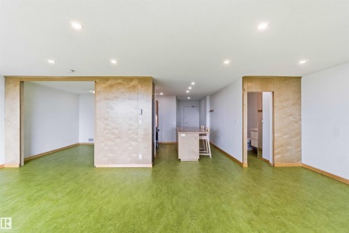 Open-concept living space featuring vibrant green flooring, recessed ceiling lighting, and a kitchen island with built-in seating - 1008 11307 99 Avenue, Edmonton, AB 