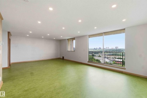 Expansive interior space featuring a full-wall window with a metal railing, recessed ceiling lighting, and a panoramic cityscape - 1008 11307 99 Avenue, Edmonton, AB 