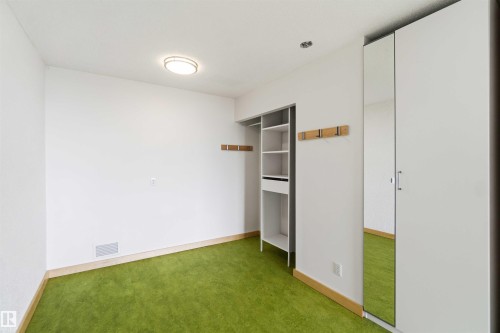 Bright room featuring green carpet flooring, white walls, built-in shelving, and a mirrored wardrobe - 1008 11307 99 Avenue, Edmonton, AB 