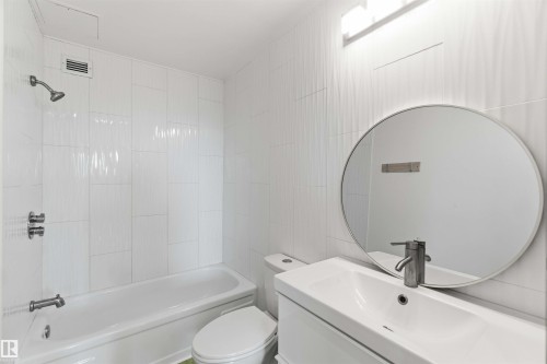 Bathroom featuring a white vanity with integrated sink, brushed nickel faucet, and circular mirror - 1008 11307 99 Avenue, Edmonton, AB 