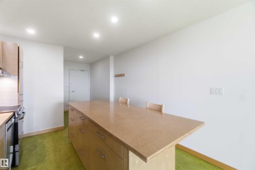 Kitchen island with integrated cabinetry and seating, featuring a stainless steel oven and range hood, white subway tile backsplash, and recessed ceiling lighting - 1008 11307 99 Avenue, Edmonton, AB 
