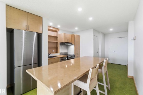 Open-concept kitchen featuring light wood cabinetry, stainless steel appliances, a built-in oven, and a wood-finish island with seating - 1008 11307 99 Avenue, Edmonton, AB 
