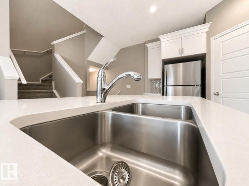 Kitchen island featuring a double basin stainless steel sink with a chrome faucet - 20104 19 Avenue, Edmonton, AB 