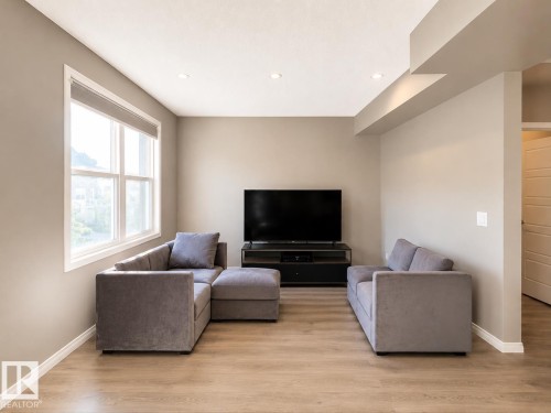 Living area featuring wood-finish flooring, recessed ceiling lighting, and a large multi-pane window - 20104 19 Avenue, Edmonton, AB 