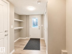 Entryway featuring wood-finish flooring, built-in shelving with coat hooks, and a white paneled door with glass insert - 