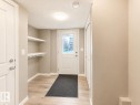 Entryway featuring wood-finish flooring, built-in shelving with coat hooks, and a white paneled door with glass insert - 20104 19 Avenue, Edmonton, AB 