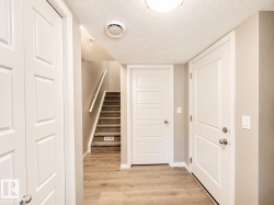 Light wood-finish flooring extending from the entryway to a carpeted staircase with a white handrail - 