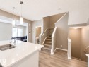 Open-concept interior featuring light wood-finish flooring, a contemporary staircase with carpeted treads, a kitchen island with a double stainless steel sink, and modern pendant lighting - 20104 19 Avenue, Edmonton, AB 