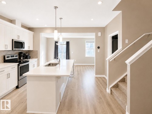 Modern kitchen featuring white cabinetry, stainless steel appliances, a large island with sink, and pendant lighting - 20104 19 Avenue, Edmonton, AB 