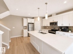 Bright kitchen featuring a large central island with dual pendant lighting, white cabinetry, integrated stainless steel appliances, a mosaic tile backsplash, and wood-finish flooring - 