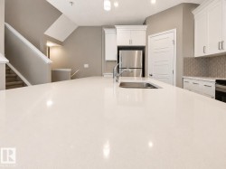 Expansive white countertop island featuring an undermount stainless steel sink and a gooseneck faucet - 