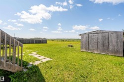 Expansive green lawn featuring a wood-sided storage shed, stone paver pathway, and wood deck stairs - 