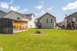 Expansive grassy backyard featuring a built-in fire pit, stone pavers, and a detached shed - 