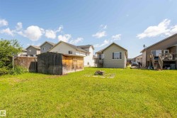 Expansive rear yard featuring green lawn, a wooden storage shed, and a stone-lined fire pit area - 
