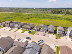 Residential street with various home styles and rooflines, set against a backdrop of expansive green fields and distant tree lines - 