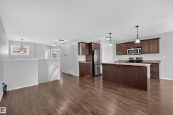 Open-concept kitchen featuring dark wood cabinetry, stainless steel appliances, a center island with a sink, and pendant lighting - 