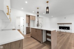 Open-concept kitchen and living area featuring a large center island with a sink, white quartz countertops, wood-finish flooring, a modern linear fireplace with a marble-look surround, and recessed lighting throughout - 