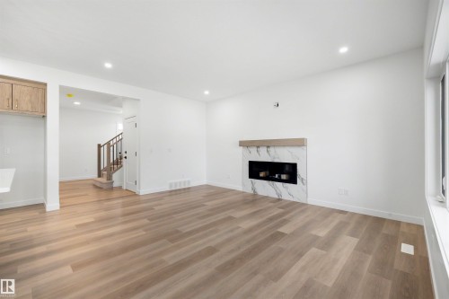 Living space featuring wood-finish flooring, recessed lighting, and a modern fireplace with a marble-look surround and wood mantel - 30 Elsinore Place, Edmonton, AB 