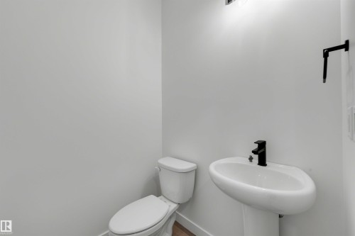 Pedestal sink with a matte black faucet, white toilet, and wood-finish flooring - 30 Elsinore Place, Edmonton, AB 
