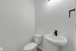 Pedestal sink with a matte black faucet, white toilet, and wood-finish flooring - 